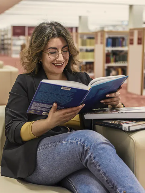 Студентка читает книгу в библиотеке и улыбается
